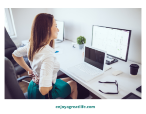 woman sitting in office at desk holding her back got pain